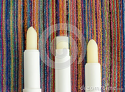 Three lip balms, sunscreen sticks on the colorful beach towel. Summer lip treatment and UV protection. Close up, flat lay Stock Photo