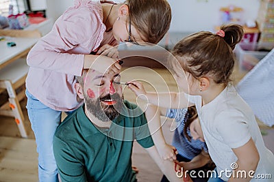 Three little girls putting on make up on their father, fathers day with daughters at home. Stock Photo