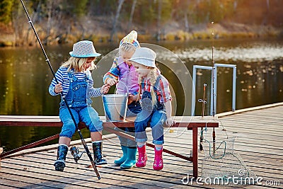 Three little happy girls brag about fish caught on a fishing pole. Fishing from a wooden pontoon Stock Photo