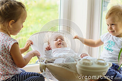 Three little Kids play near the window. Brothers and sister with the baby.Toddler kid meeting newborn sibling. Children Stock Photo