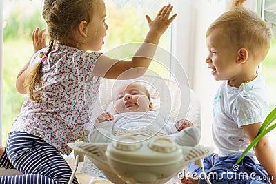 Three little Kids play near the window. Brothers and sister with the baby.Toddler kid meeting newborn sibling. Children Stock Photo