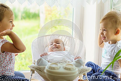 Three little Kids play near the window. Brothers and sister with the baby.Toddler kid meeting newborn sibling. Children Stock Photo
