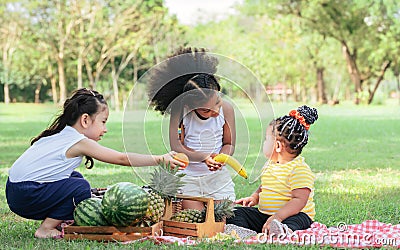 Three little mixed race kid girls smiling with happiness, fun amusement, playing, sitting for picnic and eating piece of Stock Photo