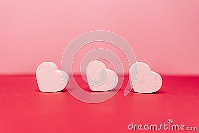 Three little white hearts situating on a line in front of the camera. Behind them there are a pink background. San Valentine`s da Stock Photo