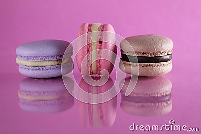 Three macaroons lilac brown chocolate lavender pink lie in a row on a pink fuchsia-colored background with reflection and a place Stock Photo