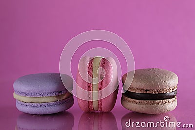 Three macaroons lilac brown chocolate lavender pink lie in a row on a pink fuchsia-colored background with reflection and a place Stock Photo