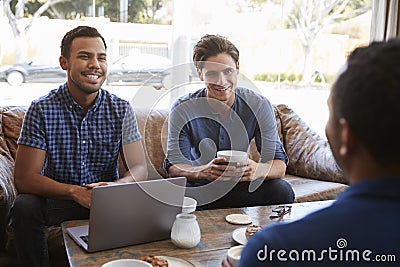 Three male friends talking over coffee at a coffee shop Stock Photo