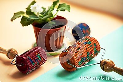 Three massager with red, orange and blue drums, metallic needles lie near a vason on a yellow-green surface. Subject and Stock Photo