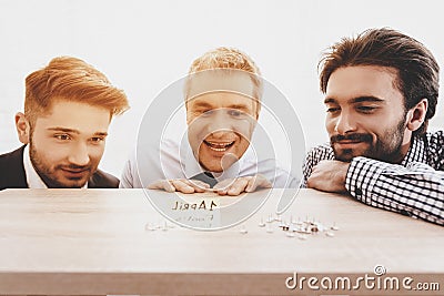 Three Men Looking at Clerical Buttons on Table. Stock Photo