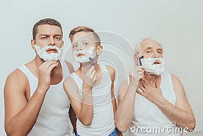 Father son and grandfather standing with shaving cream on their faces shaving with razors Stock Photo