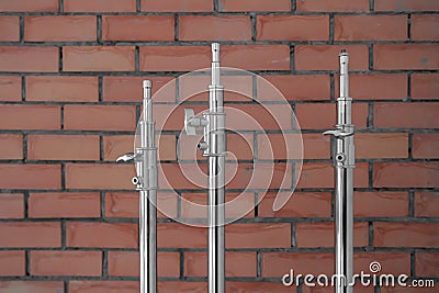 Three metal light stands with fastening mechanism above a red brick wall background Stock Photo