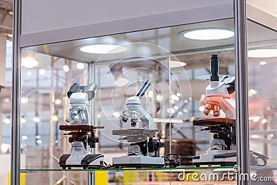 Three microscopes in glass showcase at science exhibition - laboratory equipment Editorial Stock Photo