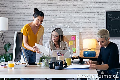 Three modern businesswomen talking and reviewing the latest work done on the digital tablet in a joint workspace Stock Photo