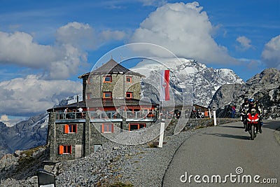 Three motorbike riders cruise past a mountaintop restaurant in sunny Dolomites. Editorial Stock Photo