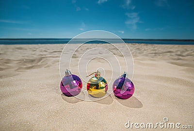 Three multi-colored, bright Christmas balls lie on the sand by the ocean, the sea. Stock Photo