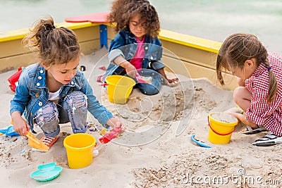 three multiethnic little children playing with plastic scoops and buckets in sandbox Stock Photo