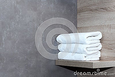 Three neatly folded white towels lie on a wooden shelf against a background of ceramic tiles. Stock Photo