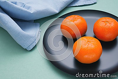 Three orange ripe mandarin citrus fruits on a table on a green tablecloth with blue towel Stock Photo