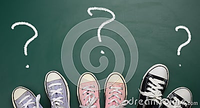 Three pairs of textile sneakers and a question mark drawn in white chalk. The concept of defining the path Stock Photo