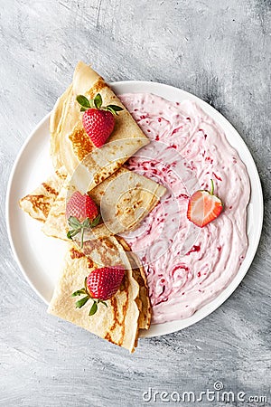 Three pancakes, sour cream and jam on a round plate on an old worn table Stock Photo