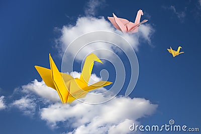 Three paper cranes flying above clouds. Stock Photo