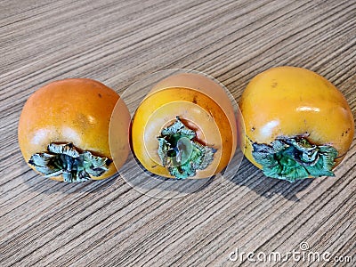 Three Persimmons on a wooden background Stock Photo