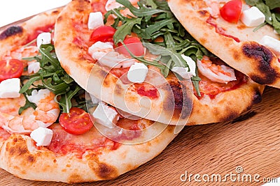 Three pizzas with prawns, tomatoes, arugula and cheese on a wooden background Stock Photo