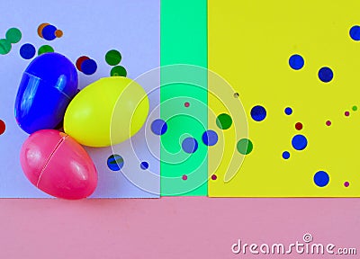 Three plastic easter eggs in blue, green, yellow and pink, with confetti on a geometric mutli-colored background Stock Photo