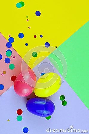 Three plastic easter eggs in blue, green, yellow and pink, with confetti on a geometric mutli-colored background Stock Photo