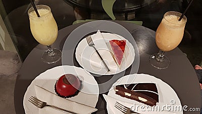 Three plates with different cakes and two fruit cocktails on round table Stock Photo