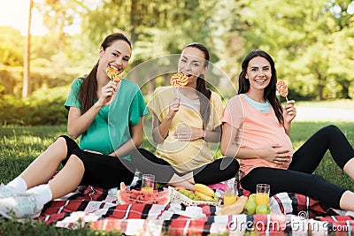 Three pregnant women posing in a picnic park with large colored candies Stock Photo