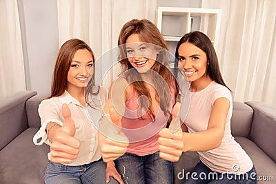 Three pretty young women sitting on couch and gesturing `LIKE` Stock Photo