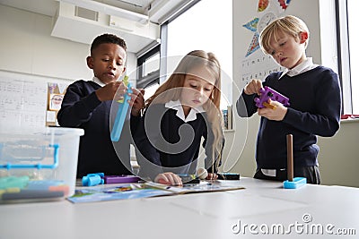 Three primary school children working together with toy construction blocks in a classroom, the girl reading instructions from a b Stock Photo