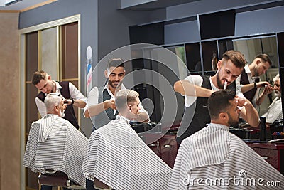 Three professional barbers trimming, cutting and styling male clients` hair. Stock Photo