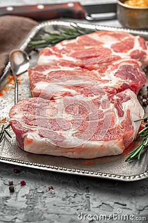 Three raw pork steaks on iron tray on light surface Stock Photo