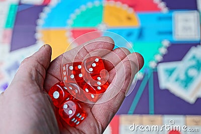 Three red dice cubes on the palm above the board game Stock Photo