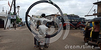 Three riders seating together at one bike with huge circle of water pipe on road Editorial Stock Photo