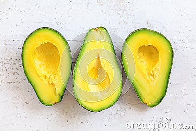 Three ripe avocado halves with bright yellow pulp on white working board, tabletop view Stock Photo