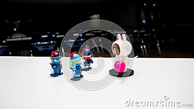Three robotic guards are assembled with blue helmets with red horns to bring down a white bear with a pink candy trespassing onsta Editorial Stock Photo