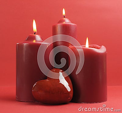 Three romantic red lit candles against a red background. Stock Photo