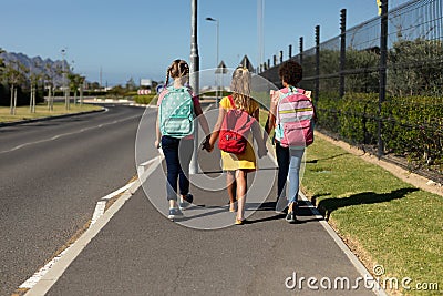 Three schoolgirls walking along a road to elementary school Stock Photo