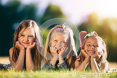 Three smiling little girls laying on the grass in the park. Stock Photo