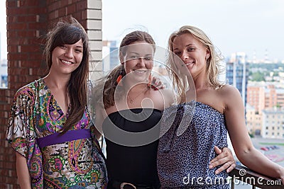 Three smiling women a friends standing and embracing together on building balcony Stock Photo