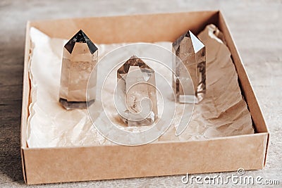 Three smoky natural quartz crystals in a kraft paper box on wooden background. Copy, empty space for text Stock Photo