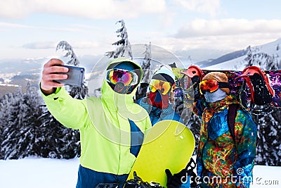 Three snowboarders taking selfie with smartphone camera at ski resort. Friends photographing for social network sharing Stock Photo