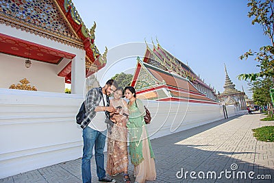 Three South Asian tourists happily stand by looking at a photo from a mobile phone behind Wat Pho during a long weekend. in Stock Photo