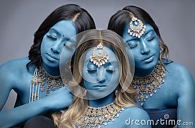 Three South Asian women painted blue and wearing gold jewellery Stock Photo