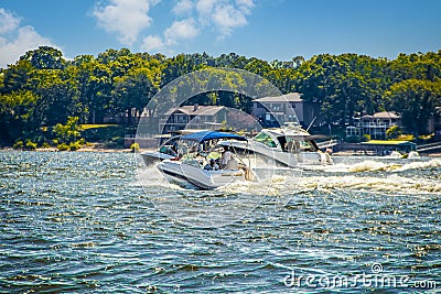 Three speedboats at lake racing in choppy water past lakeside homes and trees on nearby shore on sunny day - selective focus Stock Photo