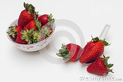 Three strawberries, one of them on a spoon and next to it a bowl with more strawberries Stock Photo