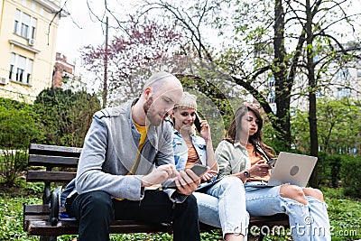 Three students on a bench in the park study talking typing on laptop notebook and writing. Education concept. Young colleagues Stock Photo